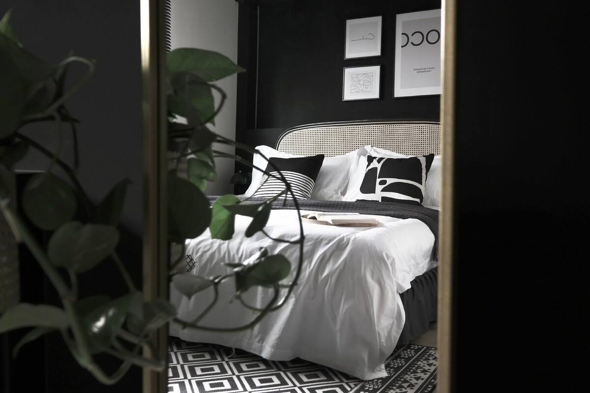 A bedroom with a bed, a black and white patterned rug, and a wall with framed pictures.