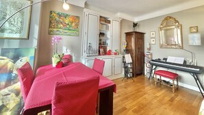 A dining area with a red table and chairs, a piano, and a cabinet with shelves. - The Artist (Cannes)
