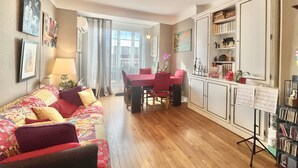 A cozy living room with a red sofa, a dining table with chairs, and a bookshelf. - The Artist (Cannes)