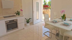 Una cocina moderna con horno empotrado, un comedor con una mesa lista para dos personas y un ventanal corredero que da a un patio exterior.