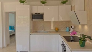 Una cocina moderna con armarios blancos, horno integrado, pileta y plantas en macetas.