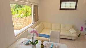 Un área de comedor con una mesa preparada para dos, un sofá y una ventana con vistas a zonas verdes.