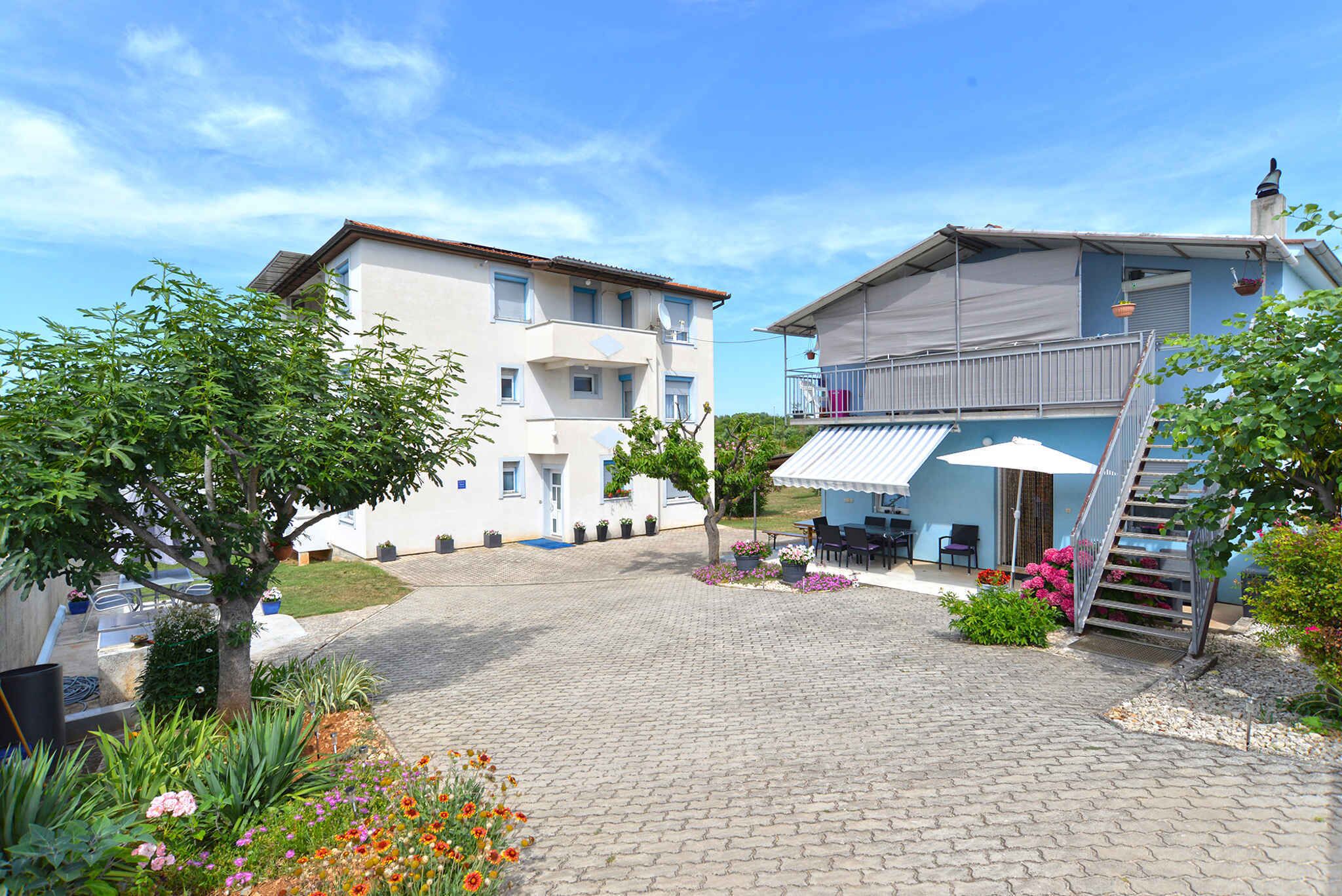 A courtyard with a paved walkway, a covered seating area, and a staircase leading to a balcony.