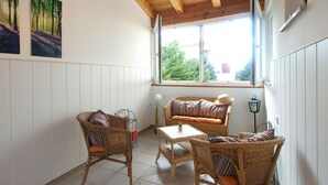 A cozy room with a wooden ceiling, a large window with a view of trees, wicker furniture, and two framed pictures on the wall. - Holiday apartment with 2 bedrooms and terrace (Banjole)