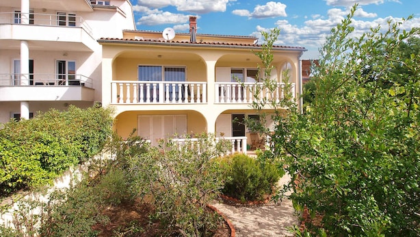 A two-story building with balconies, a satellite dish, and a garden area with shrubs and a pathway. - Holiday apartment with 2 bedrooms and terrace (Banjole)