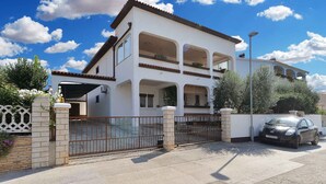 A two-story house with a gated entrance, a car parked in the driveway, and a clear blue sky with clouds. - Holiday apartment with air conditioning and large terrace (Pula)