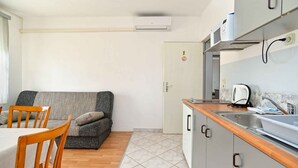 Een kleine keuken met een spoelbak, kastjes en een magnetron. Er is een eethoek met een tafel en stoelen.