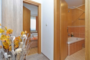 Un bagno con vasca, doccia e WC. Una porta in legno dà accesso a un'altra stanza.