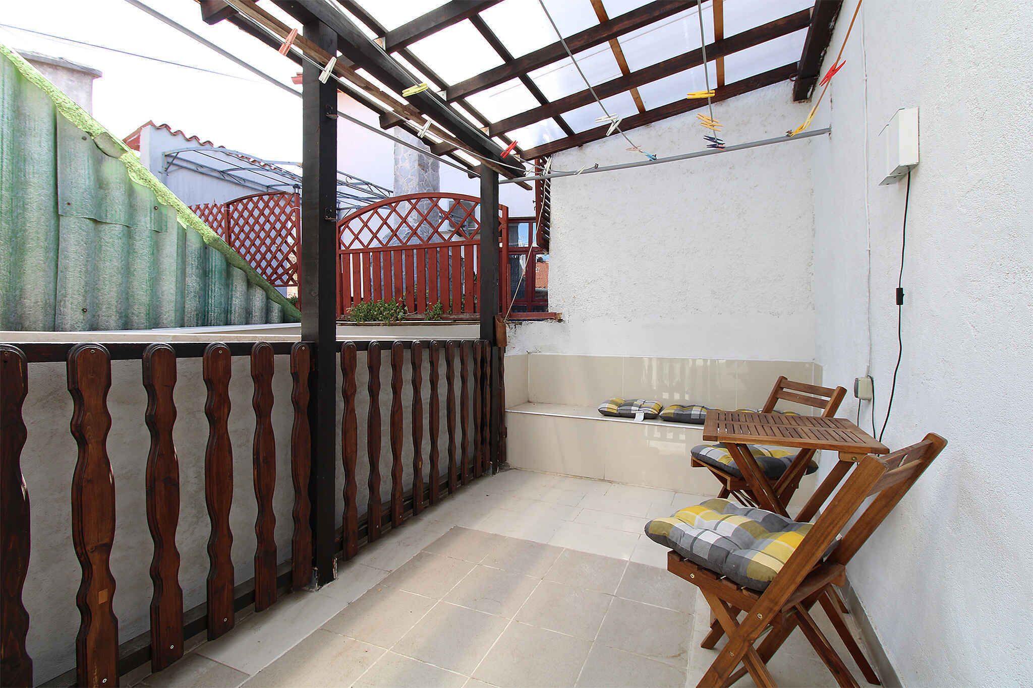 A covered patio with a wooden table and chairs, a red gate, and a white wall.