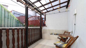 A covered patio with a wooden table and chairs, a red gate, and a white wall. - Holiday apartment with air conditioning (Pula)
