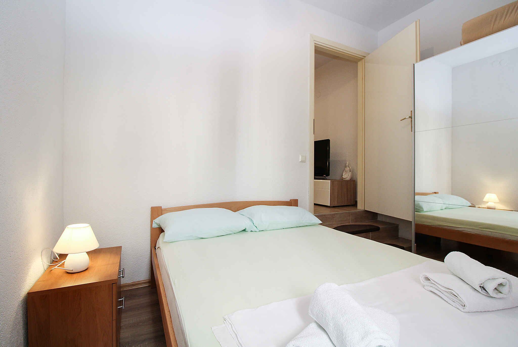 A hotel room with a bed, a nightstand with a lamp, a mirror, and a neatly made bed with towels.
