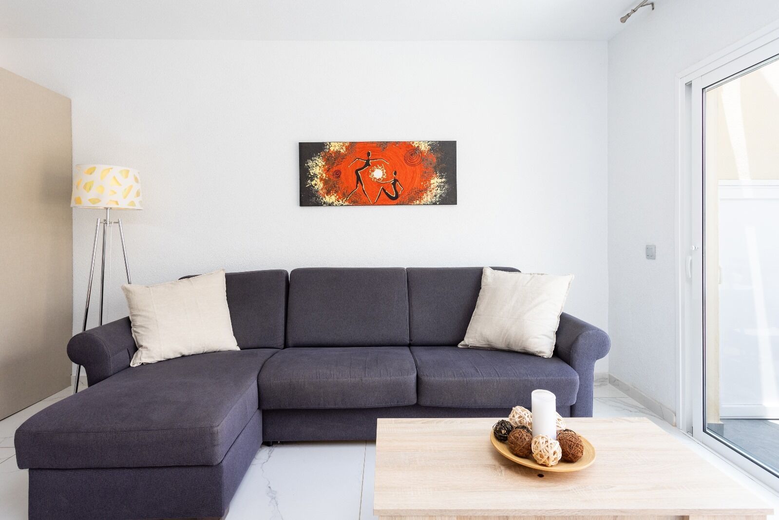 Uma sala de estar moderna com um sofá modular cinza escuro, uma luminária de chão e uma mesa de centro com objetos decorativos.