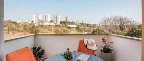 A balcony with a table, chairs, and a view of high-rise buildings in the background.