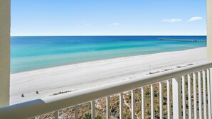 A beach view with a pier extending into the ocean, a clear sky, and a balcony railing. - Grand Panama 1101 - Stunning Sunset Views + Beach Service (Panama City Beach)