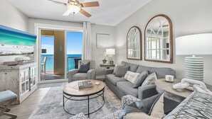 A living room with a sofa, armchairs, a coffee table, a ceiling fan, and a view of the ocean. - Grand Panama 1101 - Stunning Sunset Views + Beach Service (Panama City Beach)