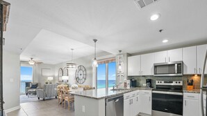 A modern kitchen with a central island, stainless steel appliances, and a view to the ocean. - Grand Panama 1101 - Stunning Sunset Views + Beach Service (Panama City Beach)