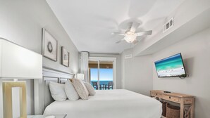 A bedroom with a bed, a desk, a TV, and a balcony view. - Grand Panama 1101 - Stunning Sunset Views + Beach Service (Panama City Beach)