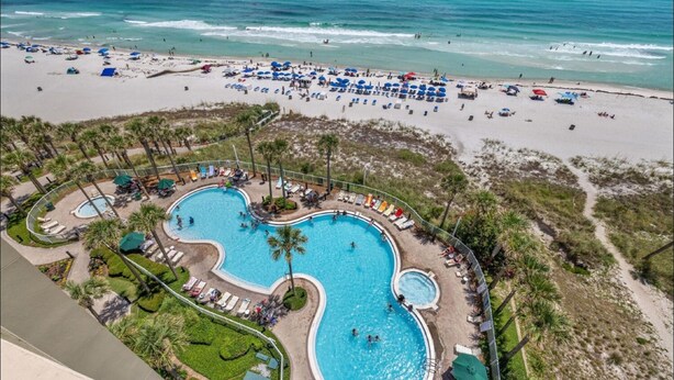 A resort with a large pool, beach area, and palm trees. - Grand Panama 1101 - Stunning Sunset Views + Beach Service (Panama City Beach)