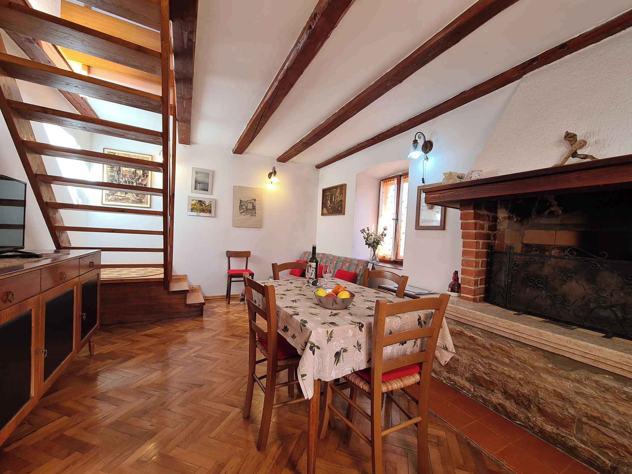 Uma sala de jantar com mesa de madeira, cadeiras e lareira. Escada leva a um andar superior.