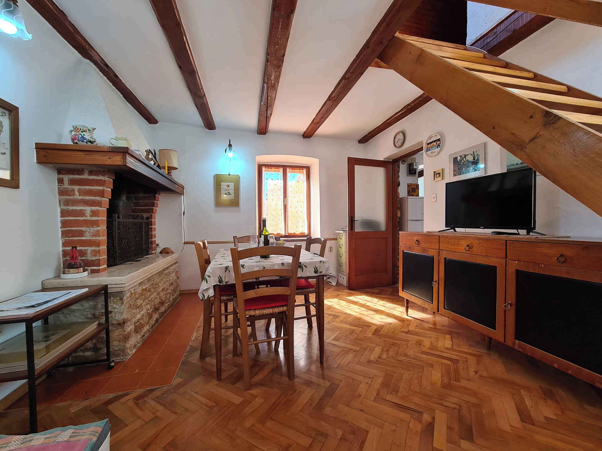 A cozy dining area with a wooden table and chairs, a brick fireplace, and a television on a wooden cabinet.
