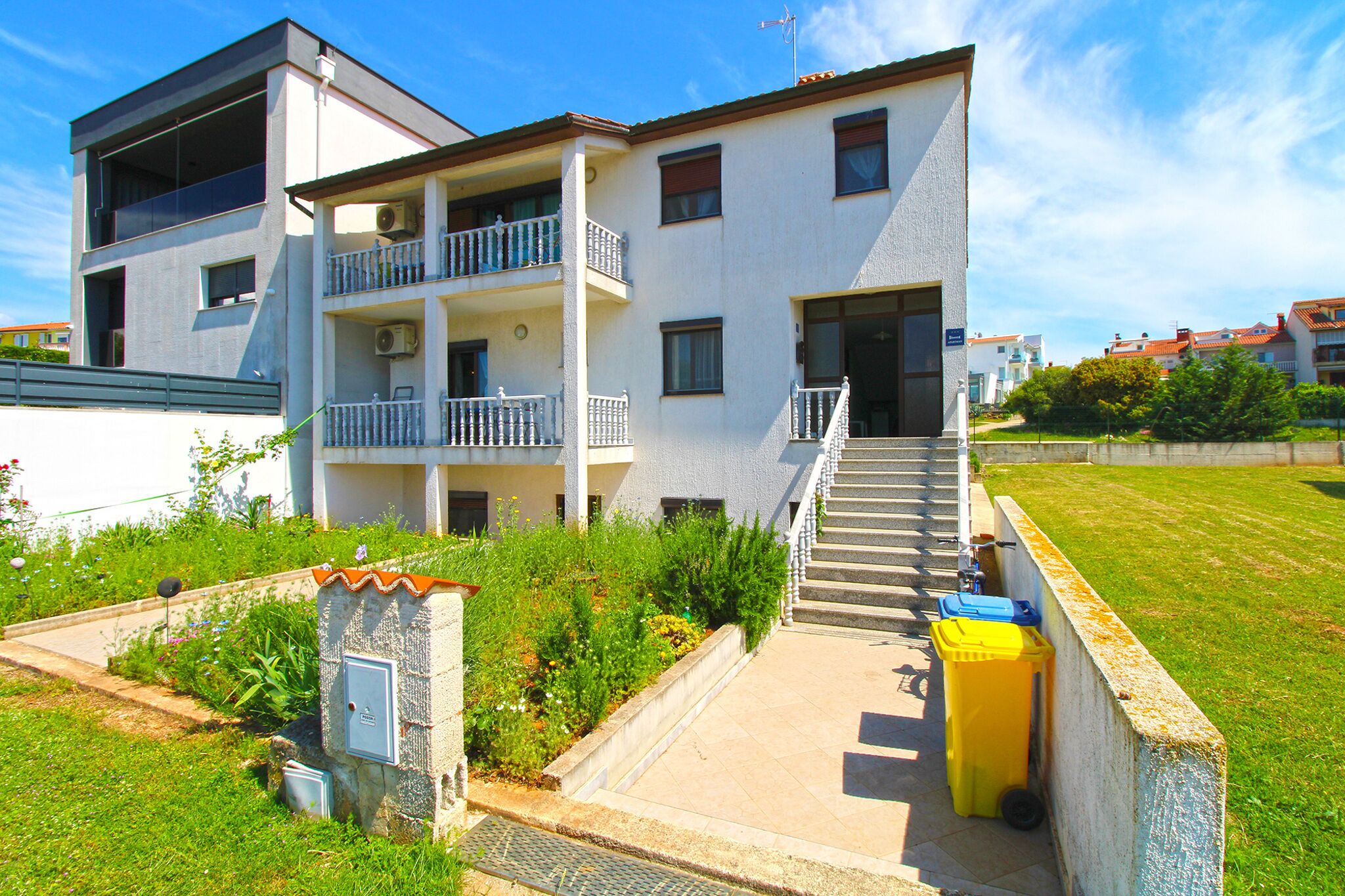 A modern two-story building with balconies, a staircase, and a small garden area.
