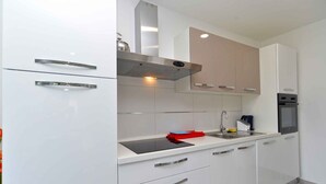 A modern kitchen with white cabinets, a stainless steel range hood, a built-in oven, and a black induction cooktop. - Holiday home with swimming pool on a large estate (Pula)