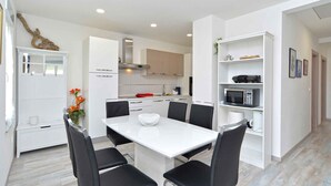 A modern kitchen with white cabinets, a white dining table with four chairs, and a microwave on a white shelf. - Holiday home with swimming pool on a large estate (Pula)
