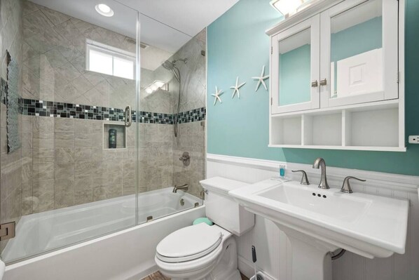 A bathroom with a glass-enclosed shower, a white toilet, and a sink with a mirror above.
