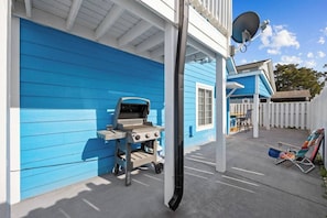 Een blauw huis met een barbecue, een schotelantenne en een overdekte patio met lounge fauteuils.