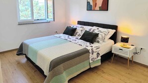 A bedroom with a bed, a nightstand, a lamp, a window, and a wall art piece. - Holiday apartment with air conditioning with terrace in modern apartment (Pula)