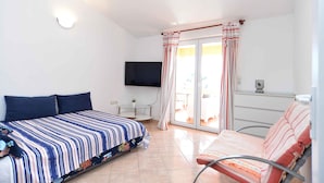 Un dormitorio con cama, una silla, un televisor y un ventanal corredera que da a un balcón.