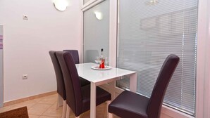 Un comedor con una mesa blanca y cuatro sillas oscuras, una botella de vino tinto y dos copas sobre la mesa.