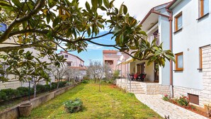 A courtyard with a stone pathway, a small garden, and a building with a balcony. - Holiday apartment with air conditioning (Pula)