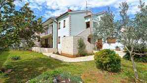 A two-story house with a stone facade, a balcony, and a well-maintained garden with various plants and a small tree. - Holiday apartment with air conditioning (Pula)