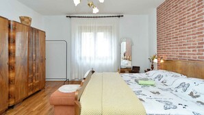 A bedroom with a wooden wardrobe, a bed with a patterned bedspread, a bedside table, and a hanging light fixture. - Holiday apartment with air conditioning (Pula)