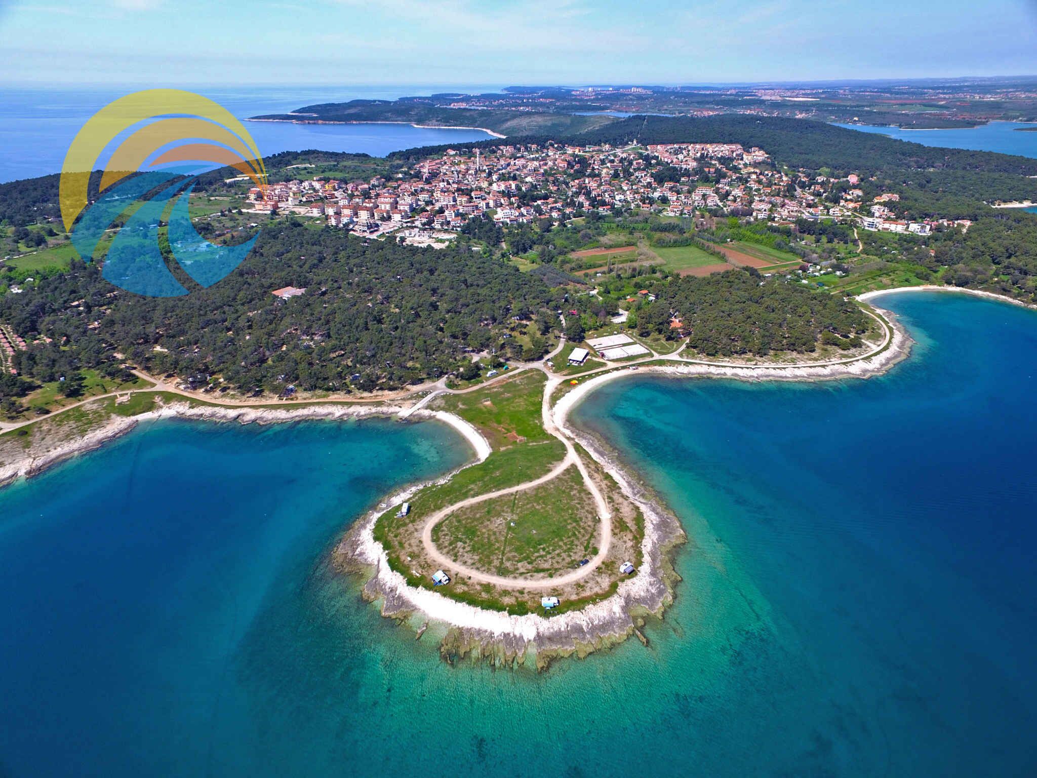 An aerial view of a coastal town with a prominent bay, a small island with a circular road, and a dense residential area in the background.