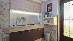 A kitchen with a stone wall, wooden cabinets, a sink, and a trash bin. - Holiday apartment with air conditioning (Premantura)