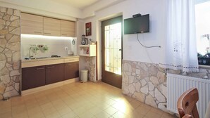 A kitchen with stone walls, a TV mounted above the counter, and a window with curtains. - Holiday apartment with air conditioning (Premantura)
