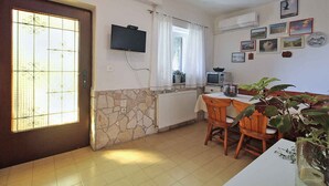 A kitchen with a stone wall, a white radiator, a TV mounted on the wall, and a dining area with wooden chairs and a table. - Holiday apartment with air conditioning (Premantura)
