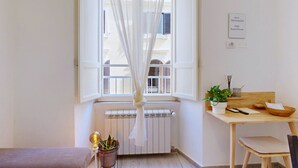 Une pièce avec une fenêtre, un radiateur, une table avec une plante, une chaise et un lit.