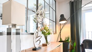Un comptoir d’accueil moderne au design minimaliste, agrémenté d’un vase en verre transparent contenant des fleurs, d’un numéro décoratif en métal et d’une lampe élégante.
