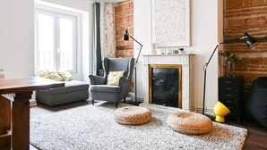 Un salon avec un canapé gris, une cheminée, un mur en briques et une grande fenêtre.