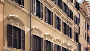 A yellow vintage car parked in front of a building with multiple windows and a sign indicating a hotel, restaurant, bar, and rooftop. - Casa Monti Roma (Rome)