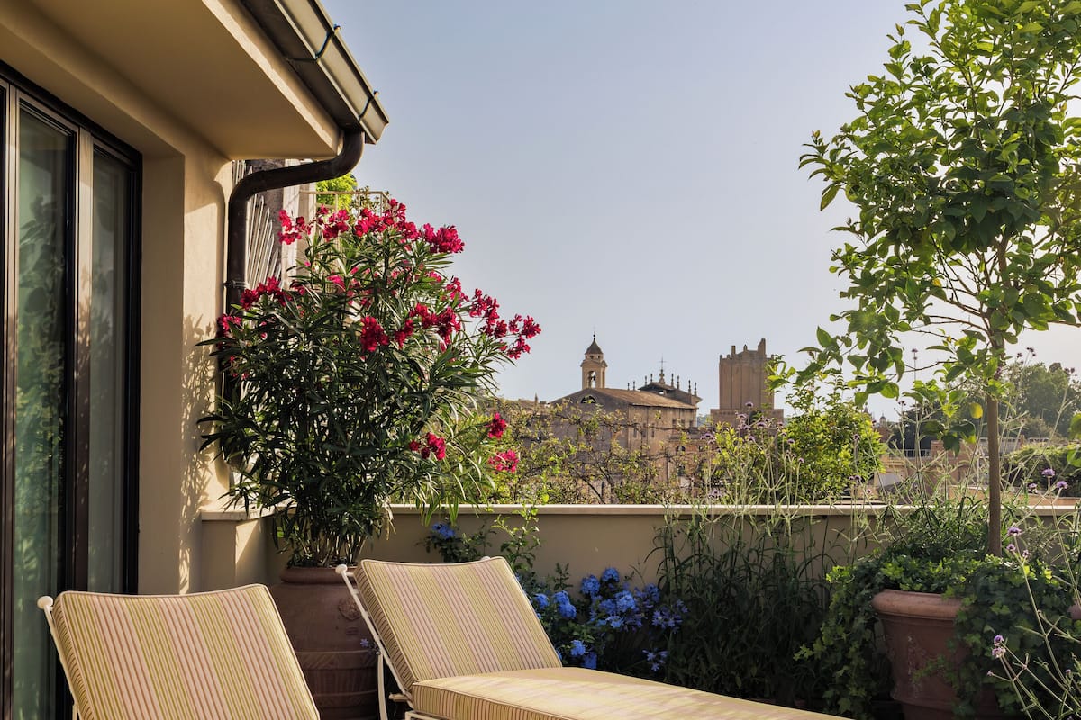 Une terrasse sur le toit avec deux chaises longues, un pot de fleurs orné de fleurs roses et, en arrière-plan, une vue sur un bâtiment historique.