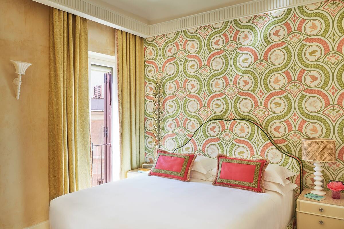Une chambre d’hôtel avec un lit, une table de chevet, une lampe et un papier peint à motifs.