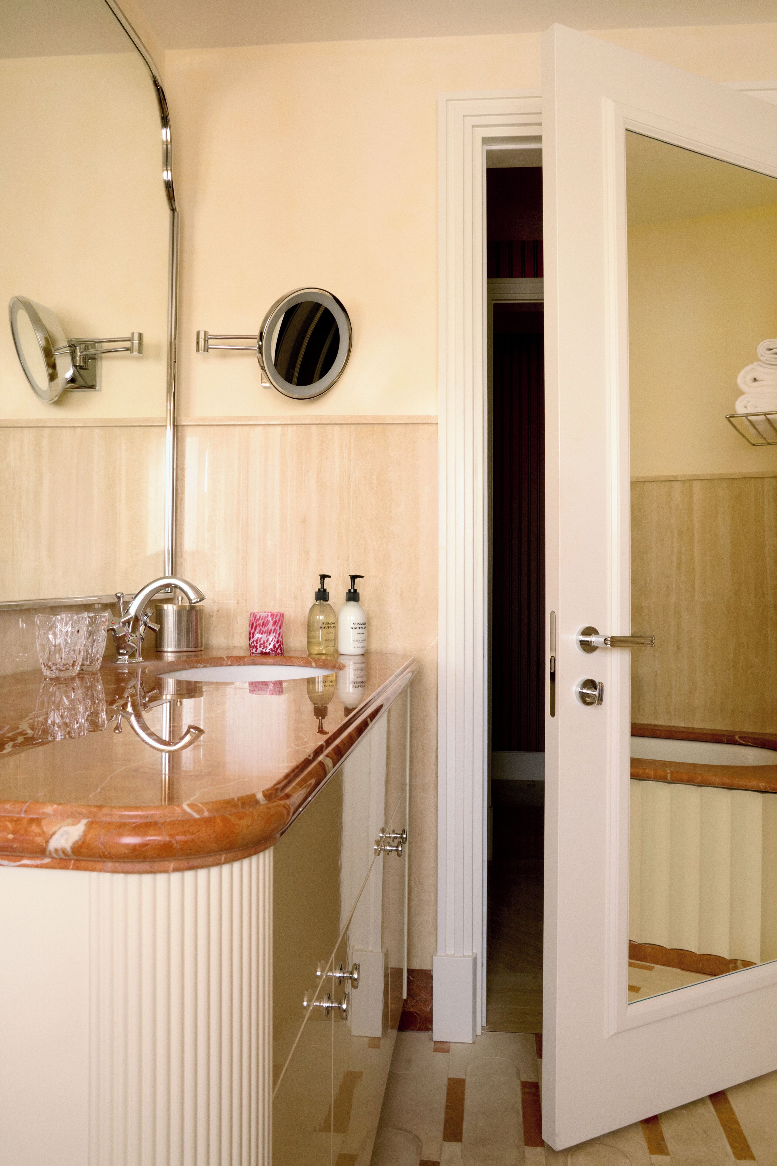 A bathroom with a marble sink, a mirror, and toiletries on the counter.