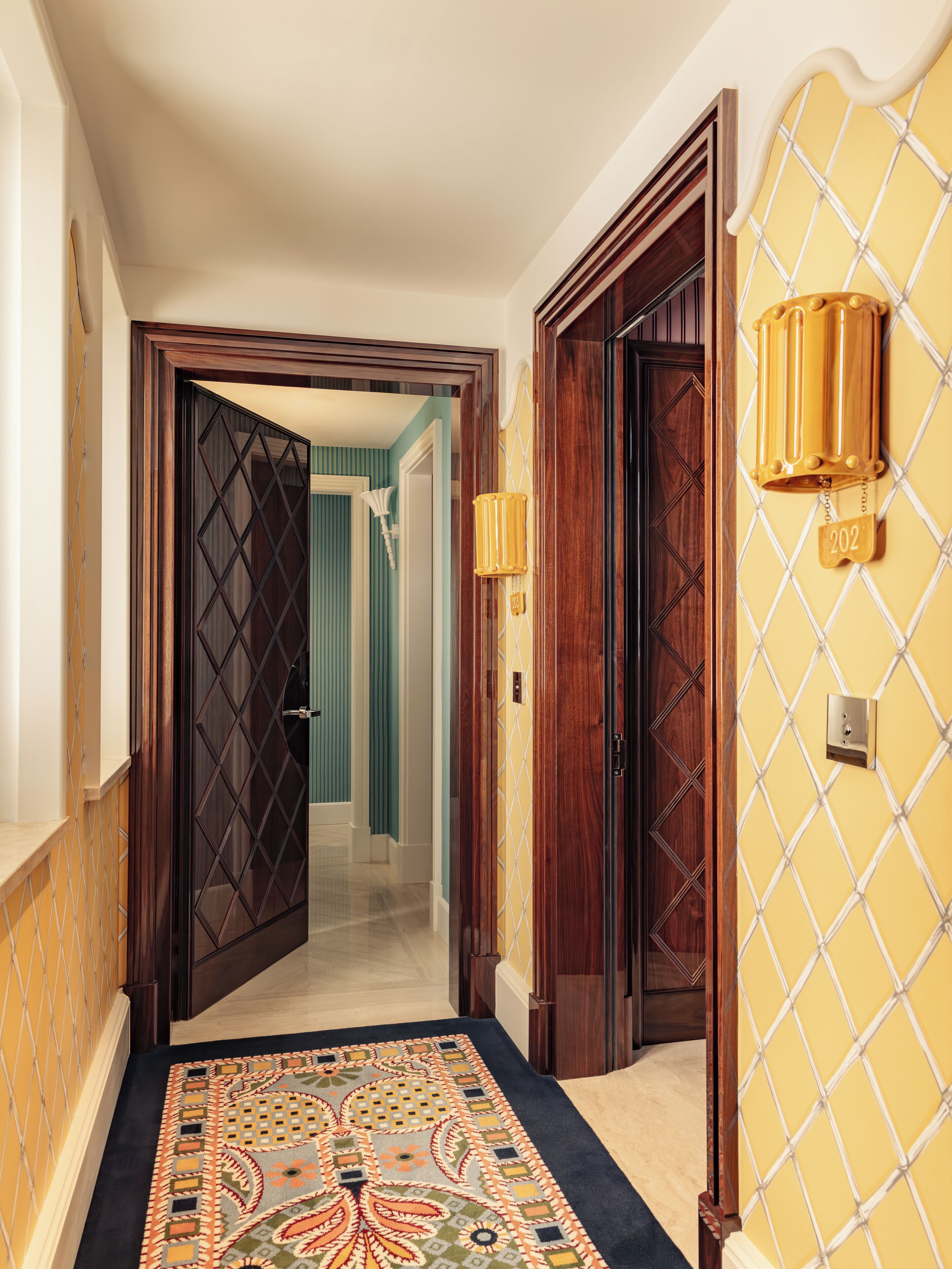 A hallway with a patterned carpet, wooden doors, and a wall-mounted light fixture.