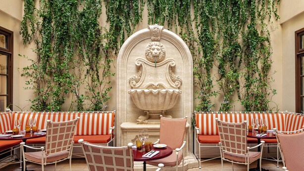 A restaurant with striped red and white upholstered booths and chairs, a stone fountain centerpiece, and lush green vines on the walls. - Casa Monti Roma (Rome)