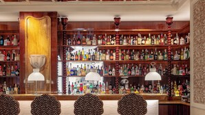 A bar area with multiple shelves of liquor bottles, a bar counter, and three patterned bar stools. - Casa Monti Roma (Rome)
