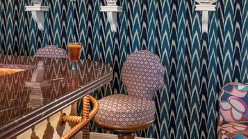 Una habitación con papel tapiz estampado, una mesa redonda con superficie de vidrio, una silla estampada y un sillón colorido.